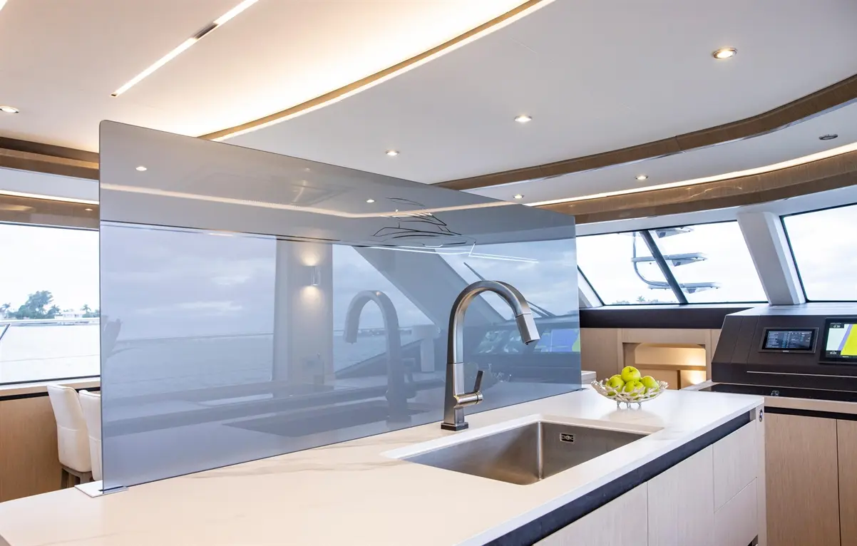 Modern yacht kitchen featuring a sleek sink, glass splashback, and bowl of green apples on a white marble countertop.